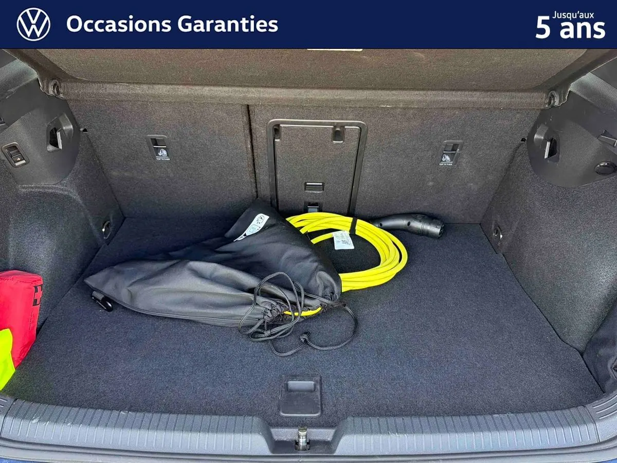 Coffre ouvert d’une Volkswagen Golf 1.5 eHybrid 2025 bleu, montrant un câble de recharge jaune et un sac noir à l’intérieur.