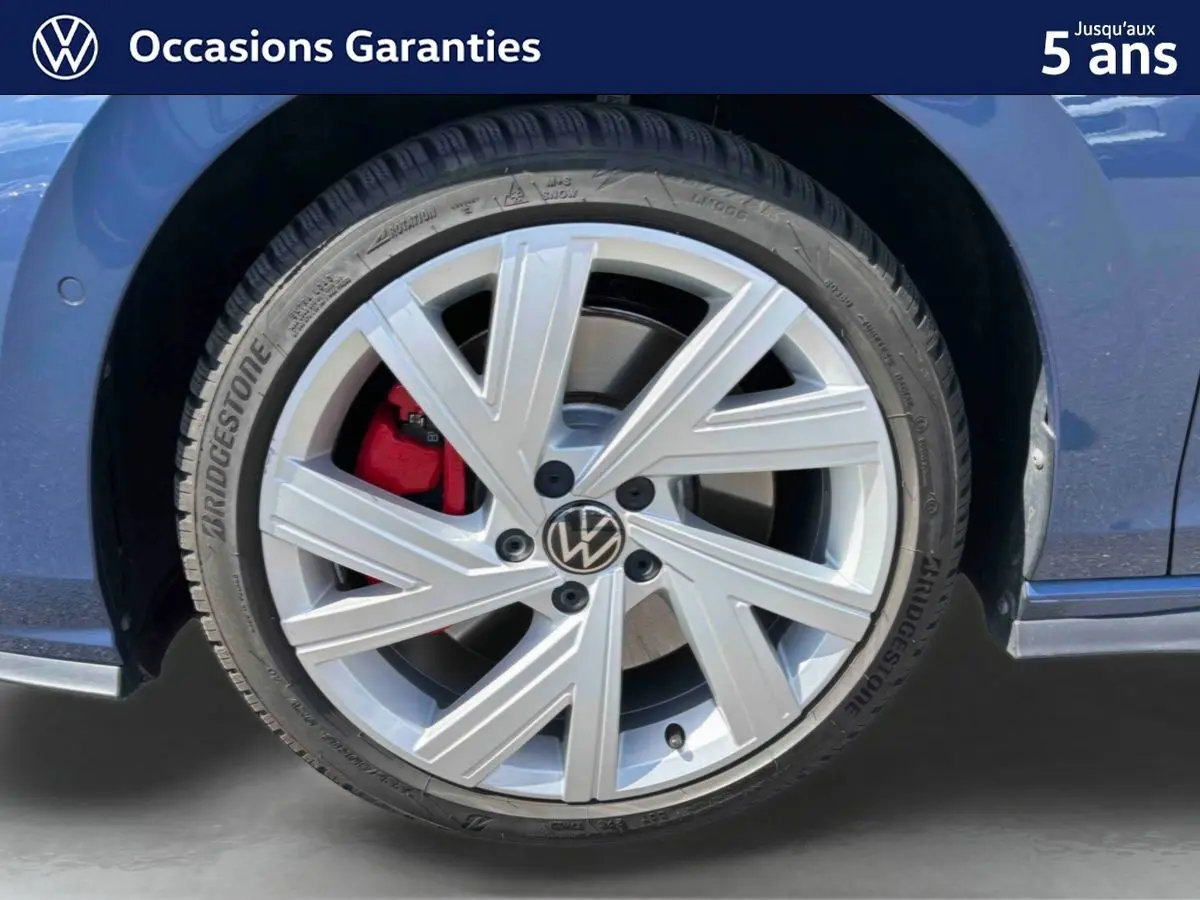 Gros plan sur la roue avant gauche d'une Volkswagen Golf 1.5 eHybrid bleue avec jante alliage 17'' et étrier de frein rouge.