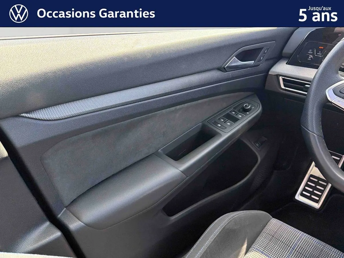 Vue intérieure côté conducteur de la Volkswagen Golf 1.5 eHybrid 2025, montrant la portière et le volant sport multifonction en cuir.