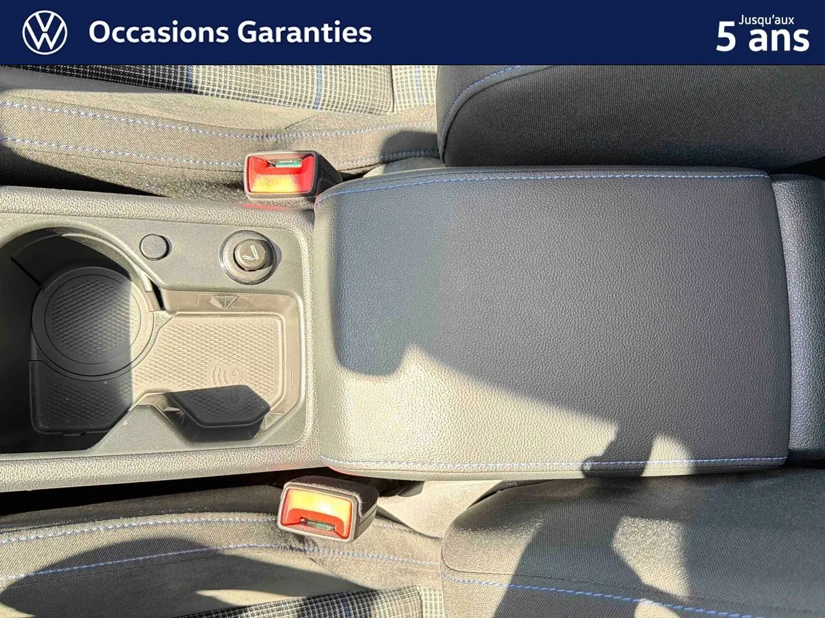 Vue rapprochée de l'accoudoir central et des porte-gobelets de la Volkswagen Golf 1.5 eHybrid 2025 en intérieur noir avec surpiqûres bleues.