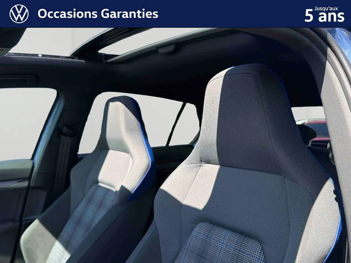 Gros plan sur les sièges sport avant gris avec surpiqûres bleues dans une Volkswagen Golf 1.5 eHybrid 2025 au toit panoramique ouvert.