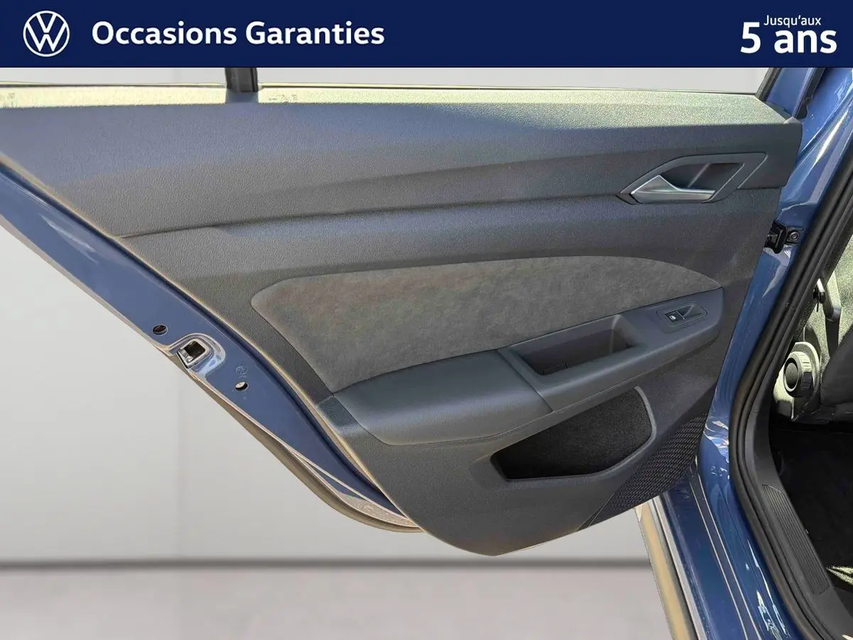 Vue rapprochée de la porte arrière gauche bleu métallisé de la Volkswagen Golf 1.5 eHybrid 2025 avec garniture intérieure grise et noire.