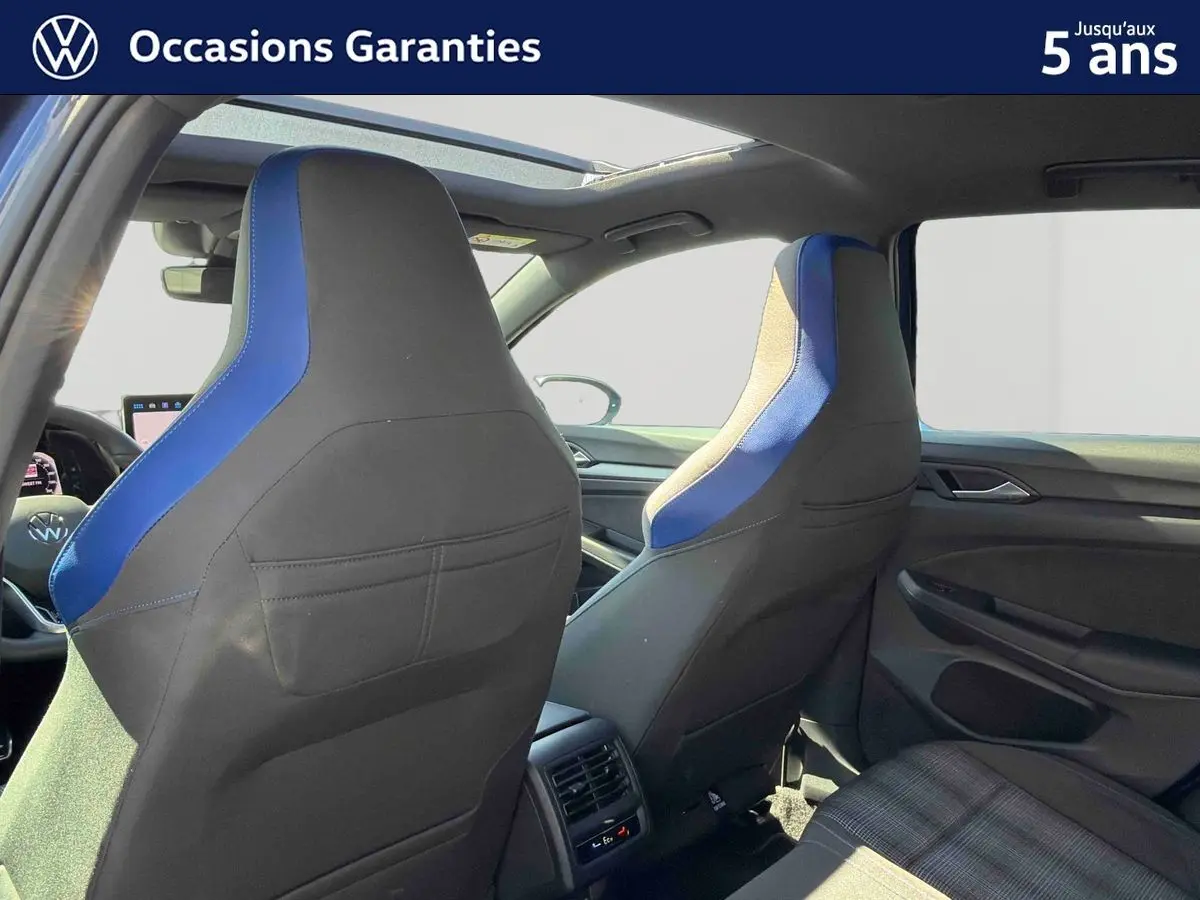 Vue intérieure arrière de la Volkswagen Golf 1.5 eHybrid 2025, sièges sport noirs avec inserts bleus et toit panoramique ouvert.
