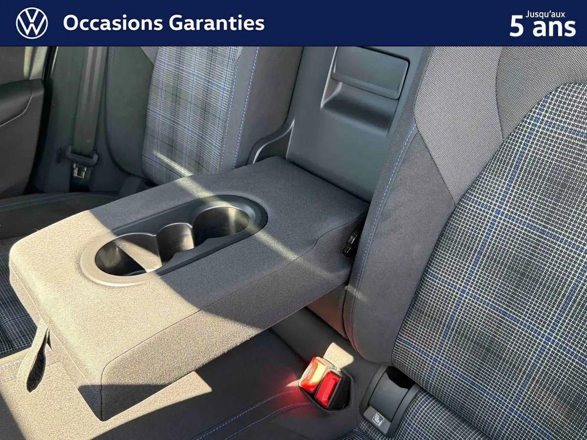 Détail de l'accoudoir central arrière avec porte-gobelets et sièges tissu à motif écossais bleu sur Volkswagen Golf 1.5 eHybrid.