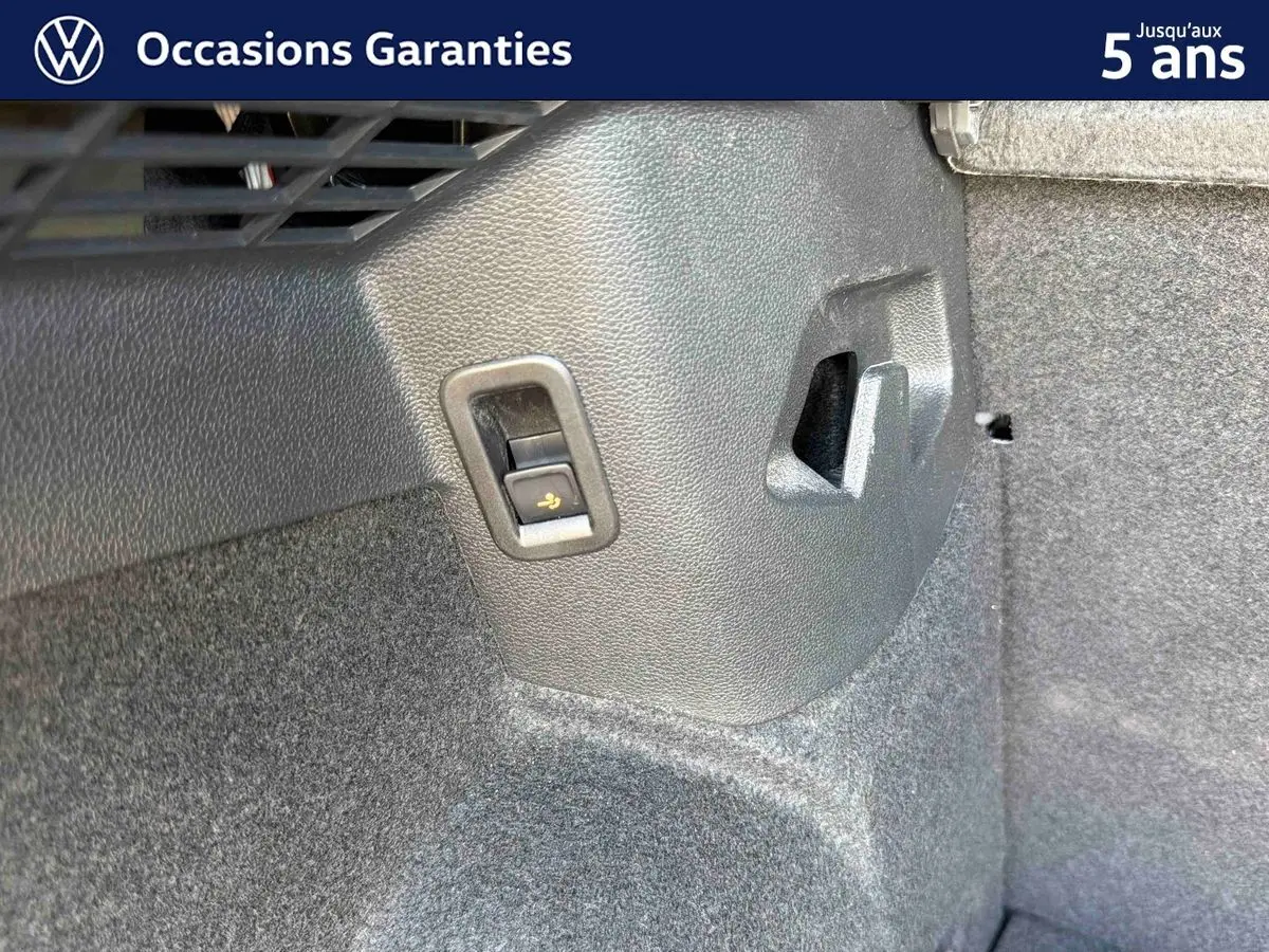 Détail intérieur du coffre de la Volkswagen Golf 1.5 eHybrid 2025, montrant un bouton de rabattement des sièges sur la paroi latérale.