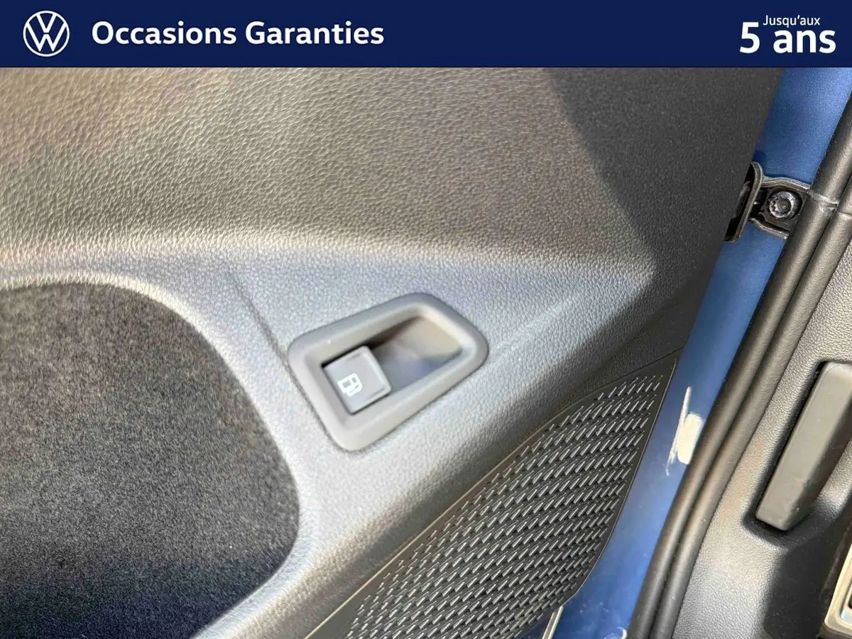 Détail de la porte arrière gauche bleu métallisé de la Volkswagen Golf 1.5 eHybrid 2025 avec commande d’ouverture de trappe à carburant.