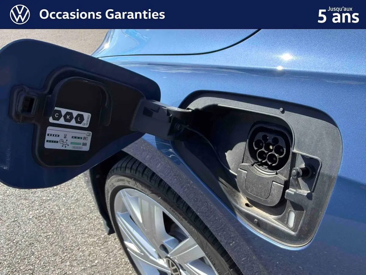 Prise de recharge ouverte côté arrière gauche sur une Volkswagen Golf 1.5 eHybrid bleue métallisée, jante alliage visible.