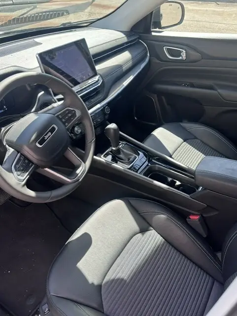 Vue intérieure côté conducteur du Jeep Compass 2025 noir, avec écran tactile central et accoudoir central visible.
