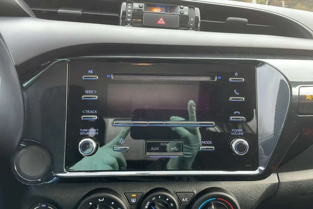 Gros plan sur la console centrale noire du Toyota Hilux 2024, avec commandes audio et climatisation visibles.