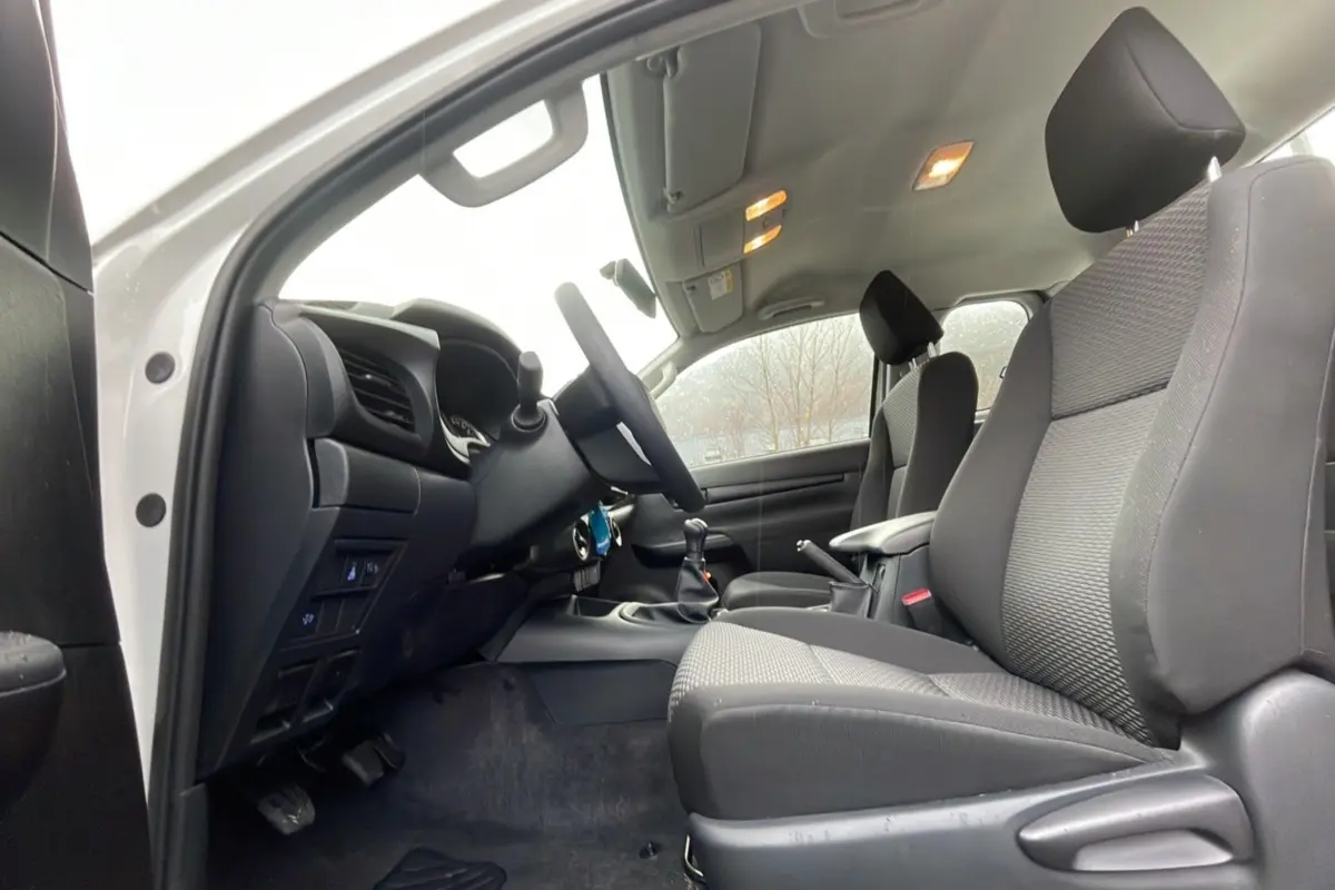 Intérieur du Toyota Hilux 4x4 2024 en vue latérale côté conducteur, sièges noirs et tableau de bord visible.