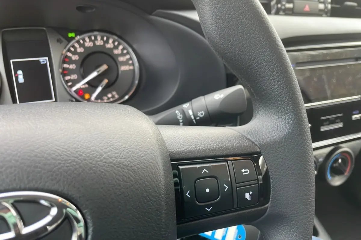Gros plan sur le volant noir du Toyota Hilux 4x4 2024 avec commandes multifonctions et tableau de bord partiel.