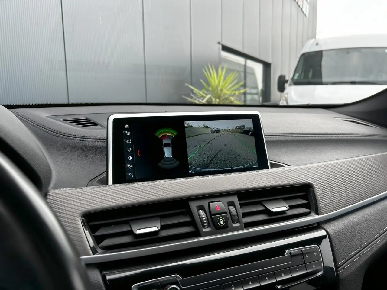 Vue du tableau de bord du BMW X2 F39 avec écran affichant la caméra de recul et les capteurs de stationnement.