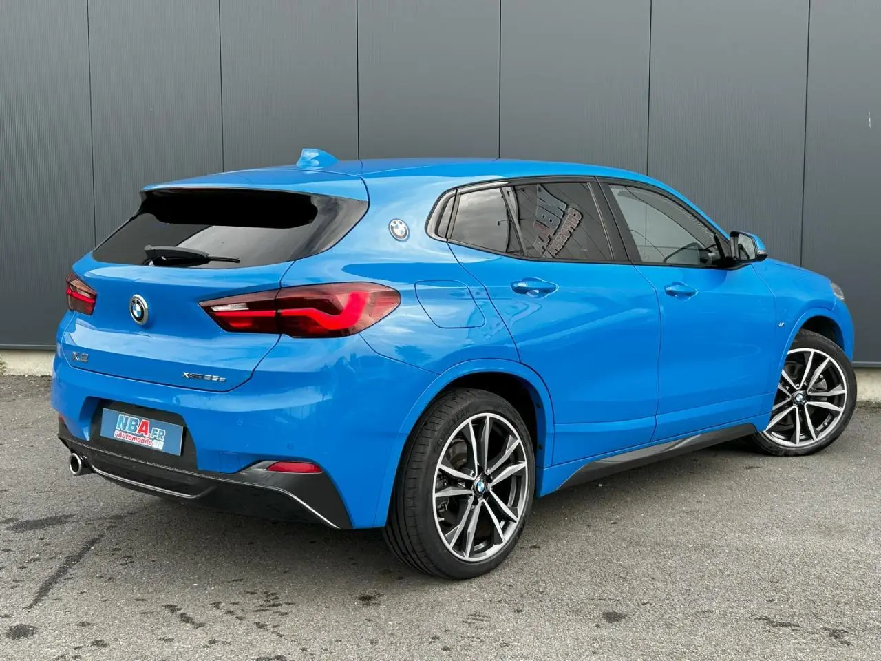 BMW X2 xDrive 25e bleu Misano vue 3/4 arrière droit avec jantes alliage bicolores et vitres teintées