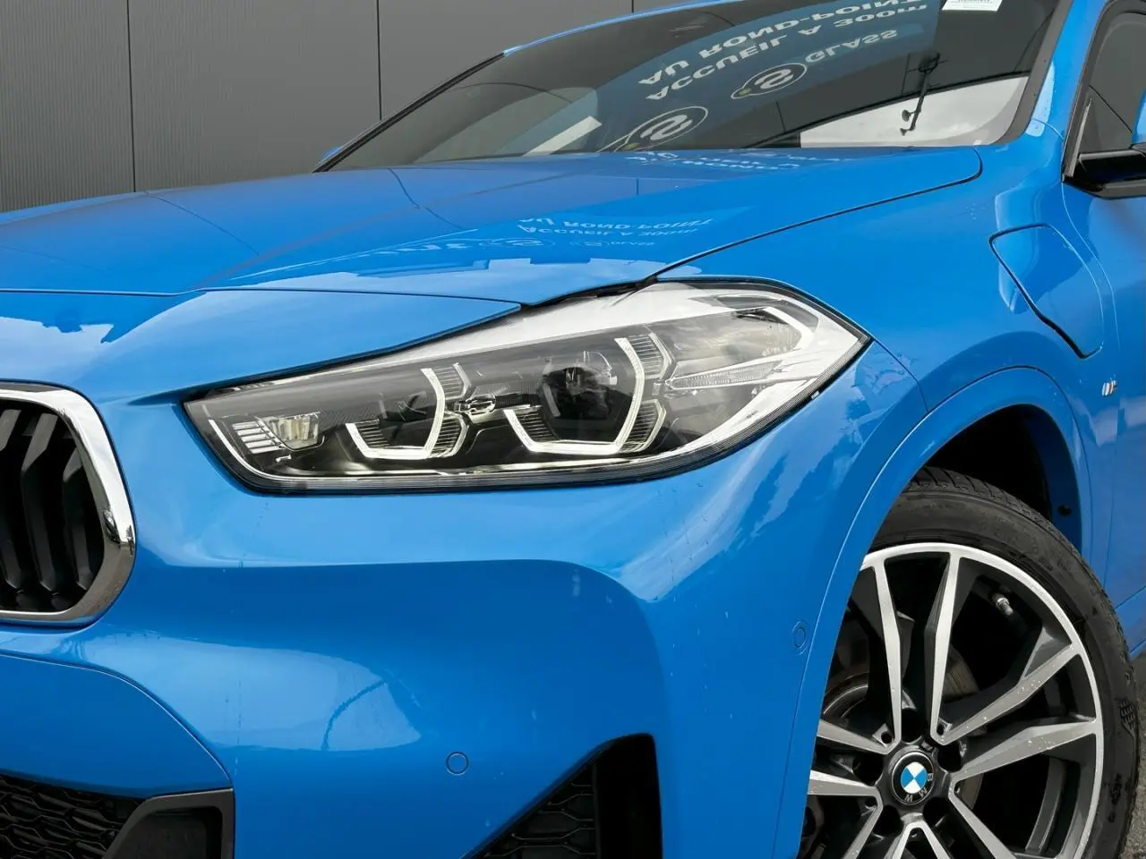 Gros plan sur l'avant droit bleu Misano du BMW X2 F39 xDrive 25e avec jante alliage bicolore et phares LED distinctifs.