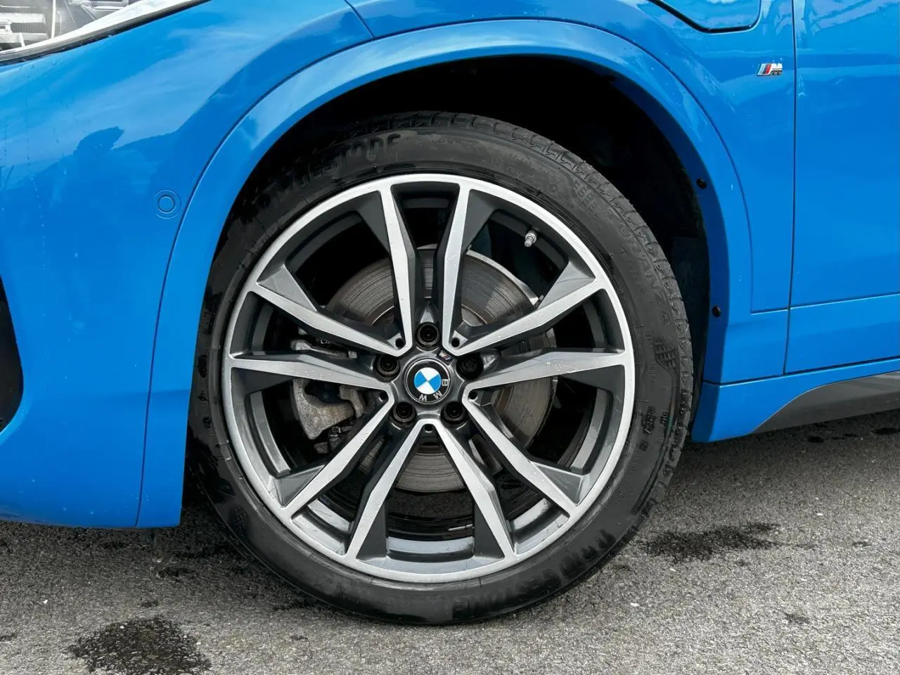 Gros plan sur la jante alliage bicolore 19 pouces côté avant gauche d'une BMW X2 Bleu Misano avec badge M Sport.