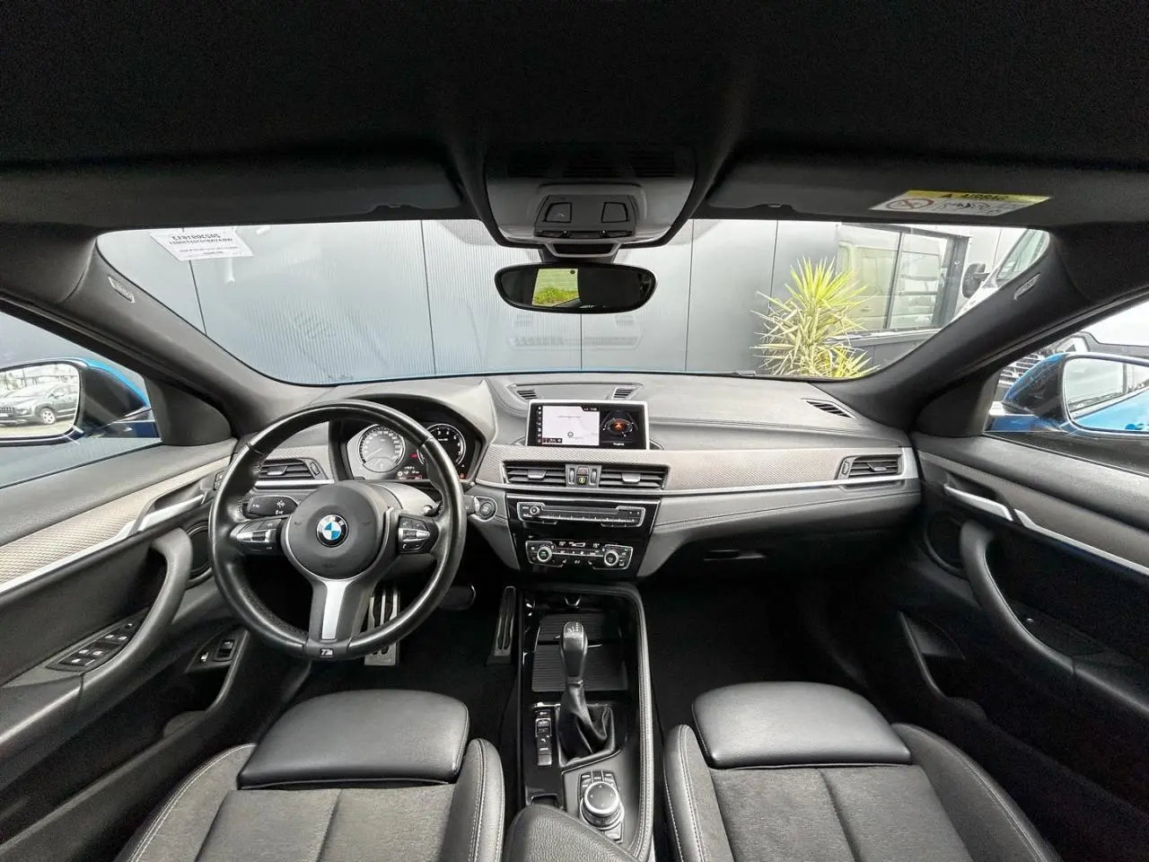 Vue intérieure frontale du BMW X2 F39 2021, tableau de bord noir avec volant M cuir et écran GPS central.