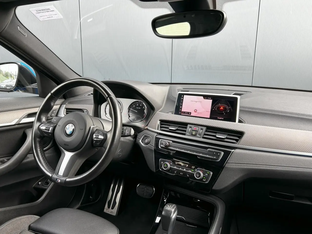 Intérieur BMW X2 F39 vu côté conducteur, volant cuir M, tableau de bord avec écran GPS et finitions grises anthracite.