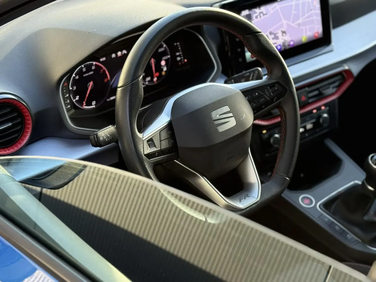 Vue rapprochée de l'intérieur de la SEAT IBIZA TSI 115 FR 2025, volant cuir avec logo SEAT et détails rouges.