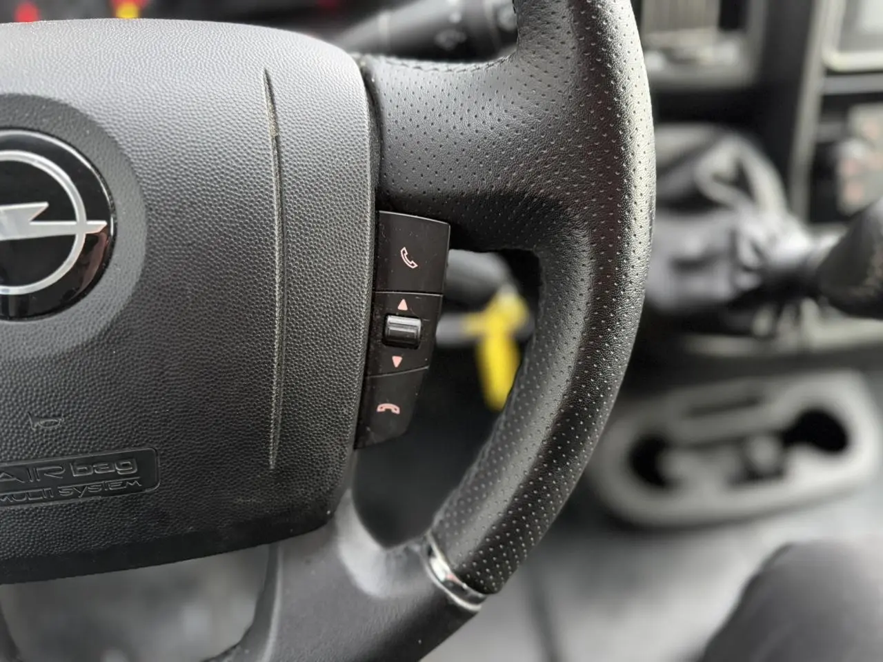 Gros plan sur le volant en cuir noir perforé de l’Opel Movano Fourgon 2024, avec commandes intégrées visibles.