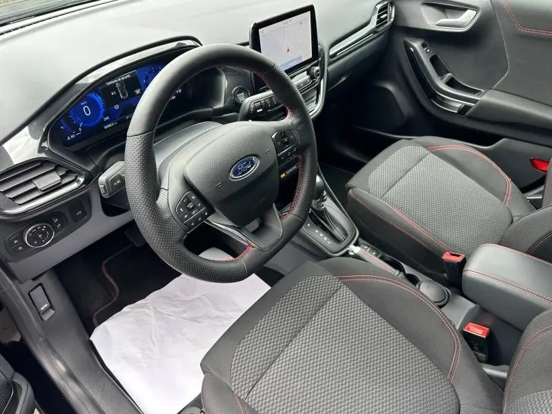 Vue intérieure côté conducteur du Ford Puma 2024 noir Agate, avec volant multifonction, écran tactile et sièges tissu à surpiqûres rouges.
