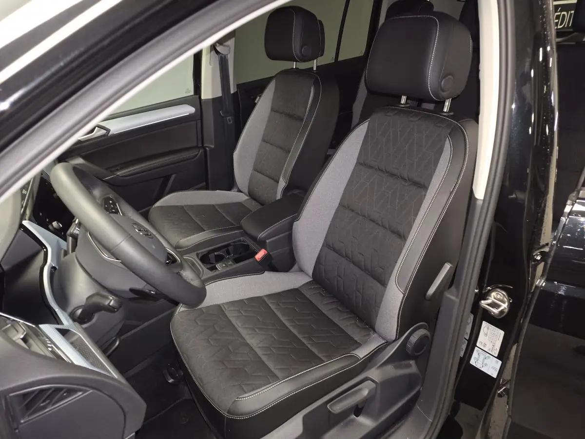 Vue intérieure côté conducteur du Volkswagen Touran noir 2025, mettant en valeur les sièges avant bi-matière gris et noir.