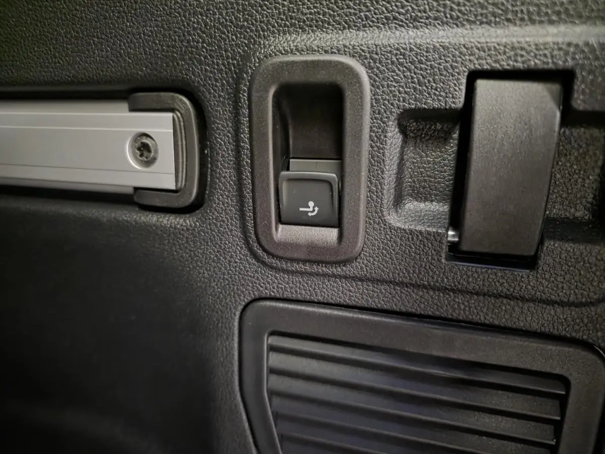 Détail du bouton de rabattement électrique des sièges arrière dans le coffre du Volkswagen Touran noir 2025.