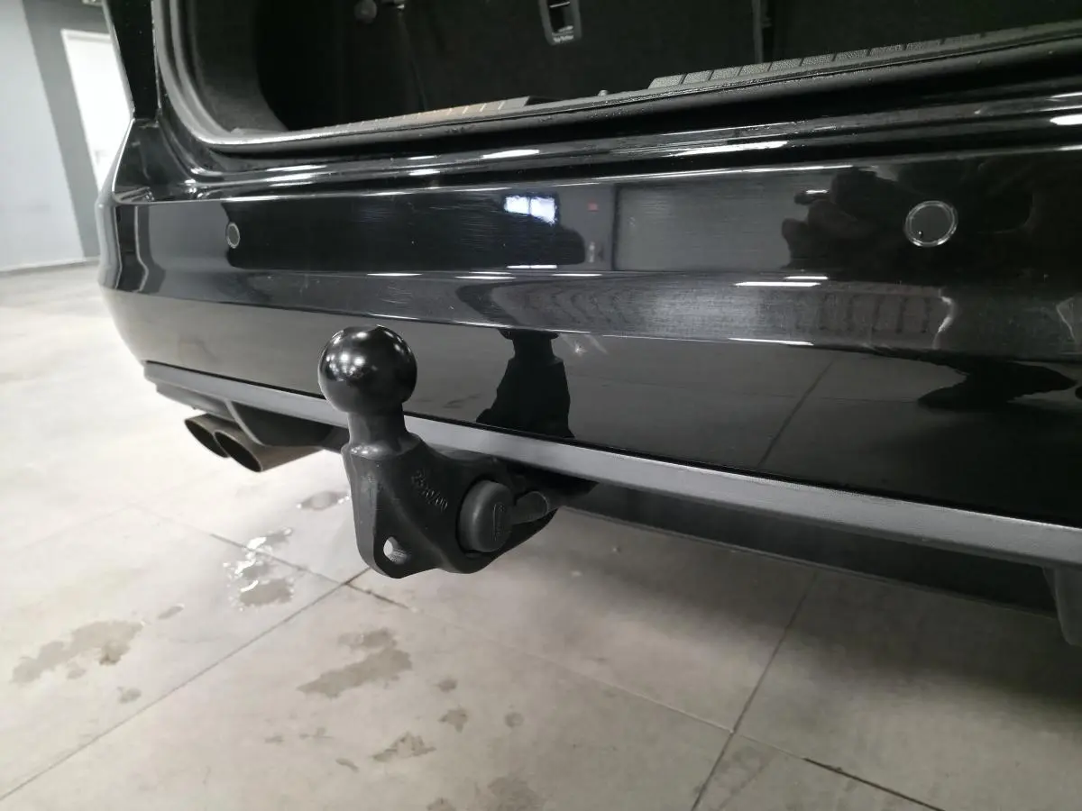 Gros plan sur l'attelage escamotable arrière du Volkswagen Touran noir, hayon ouvert, dans un garage.