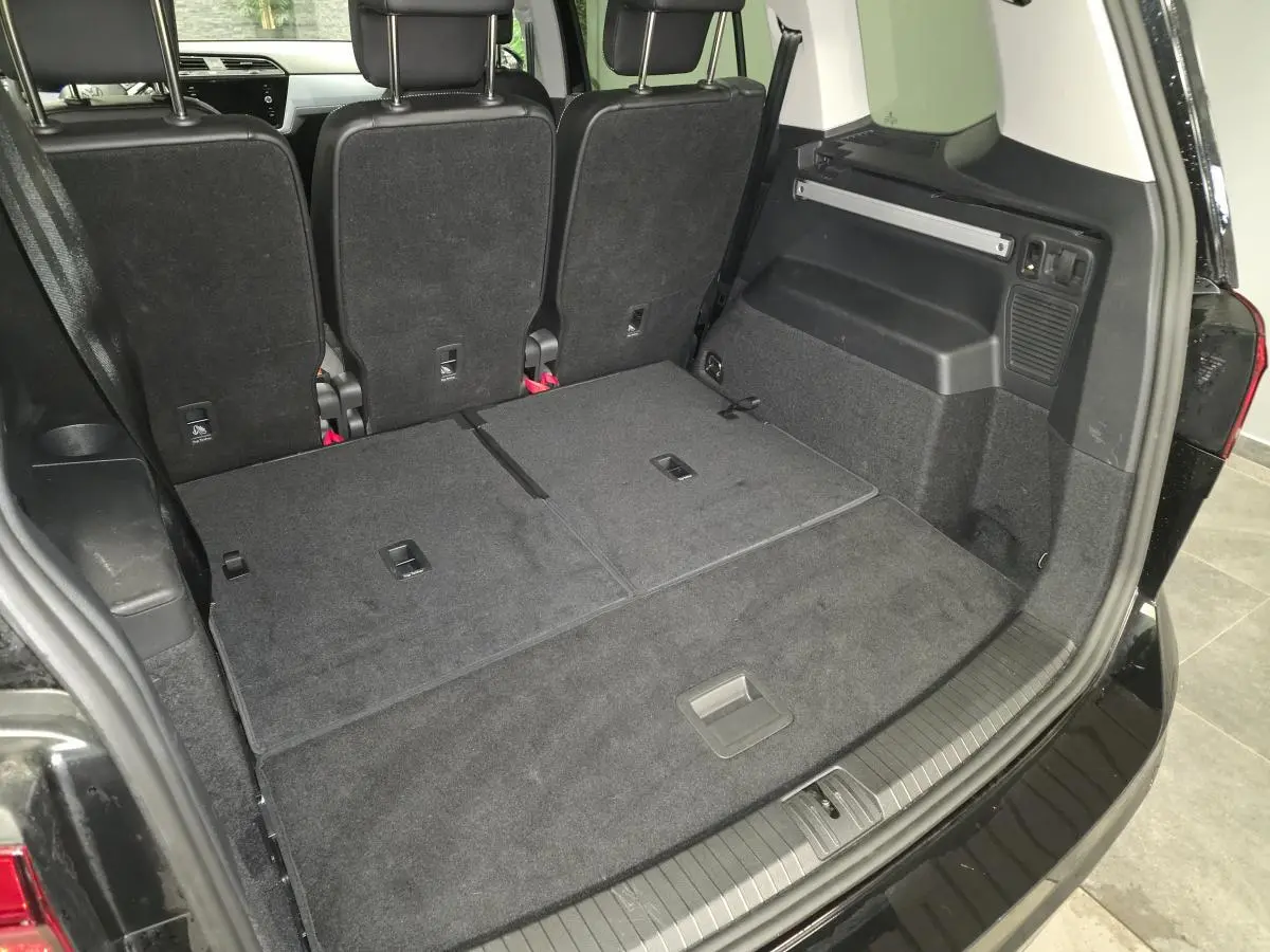 Vue arrière du coffre noir du Volkswagen Touran 2025 avec sièges rabattus et hayon ouvert montrant l'espace de chargement.