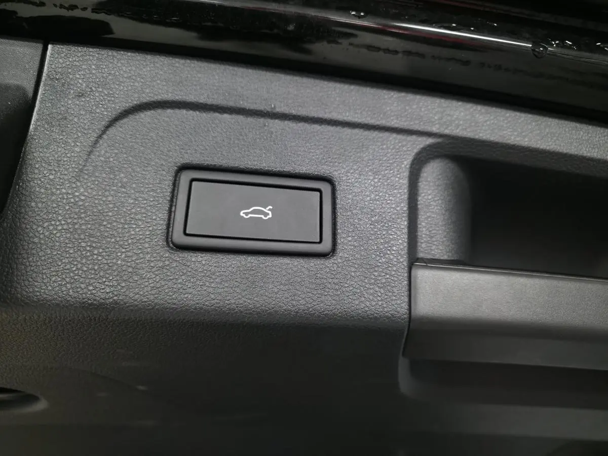 Bouton noir d'ouverture électrique du hayon sur le panneau intérieur du coffre d'un Volkswagen Touran noir.