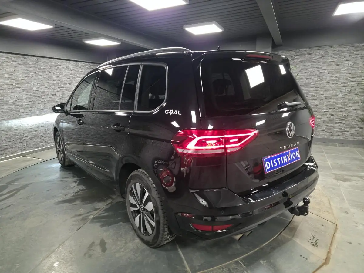 Vue 3/4 arrière droite d'un Volkswagen Touran noir intense avec hayon et crochet d'attelage escamotable visible.