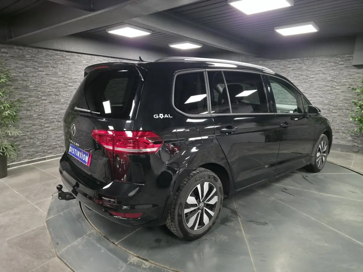 Volkswagen Touran noir 2025 en 3/4 arrière droit, hayon avec attelage escamotable et vitres surteintées.