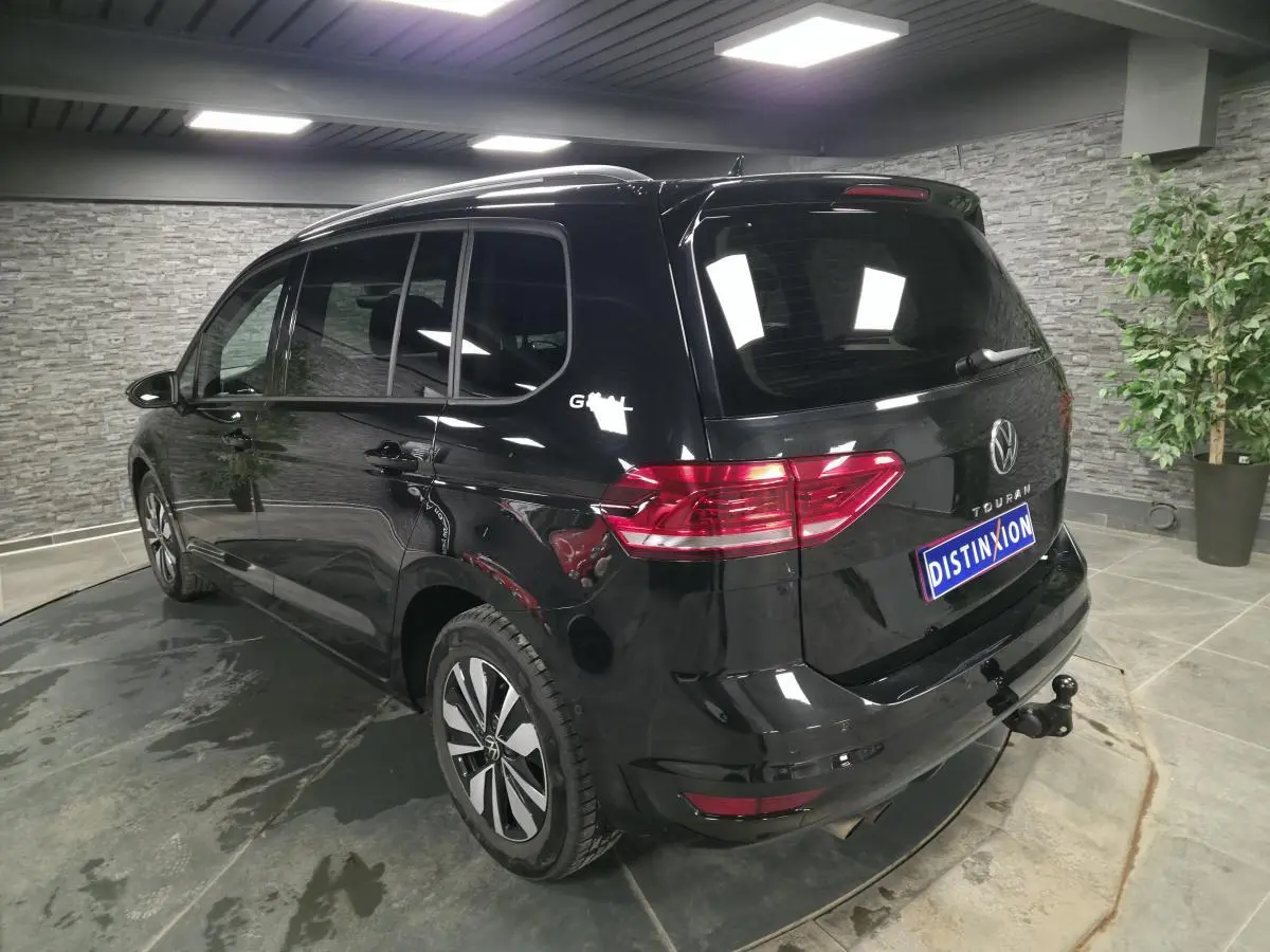 Vue 3/4 arrière droite d'un Volkswagen Touran noir avec hayon et crochet d'attelage escamotable en intérieur showroom.