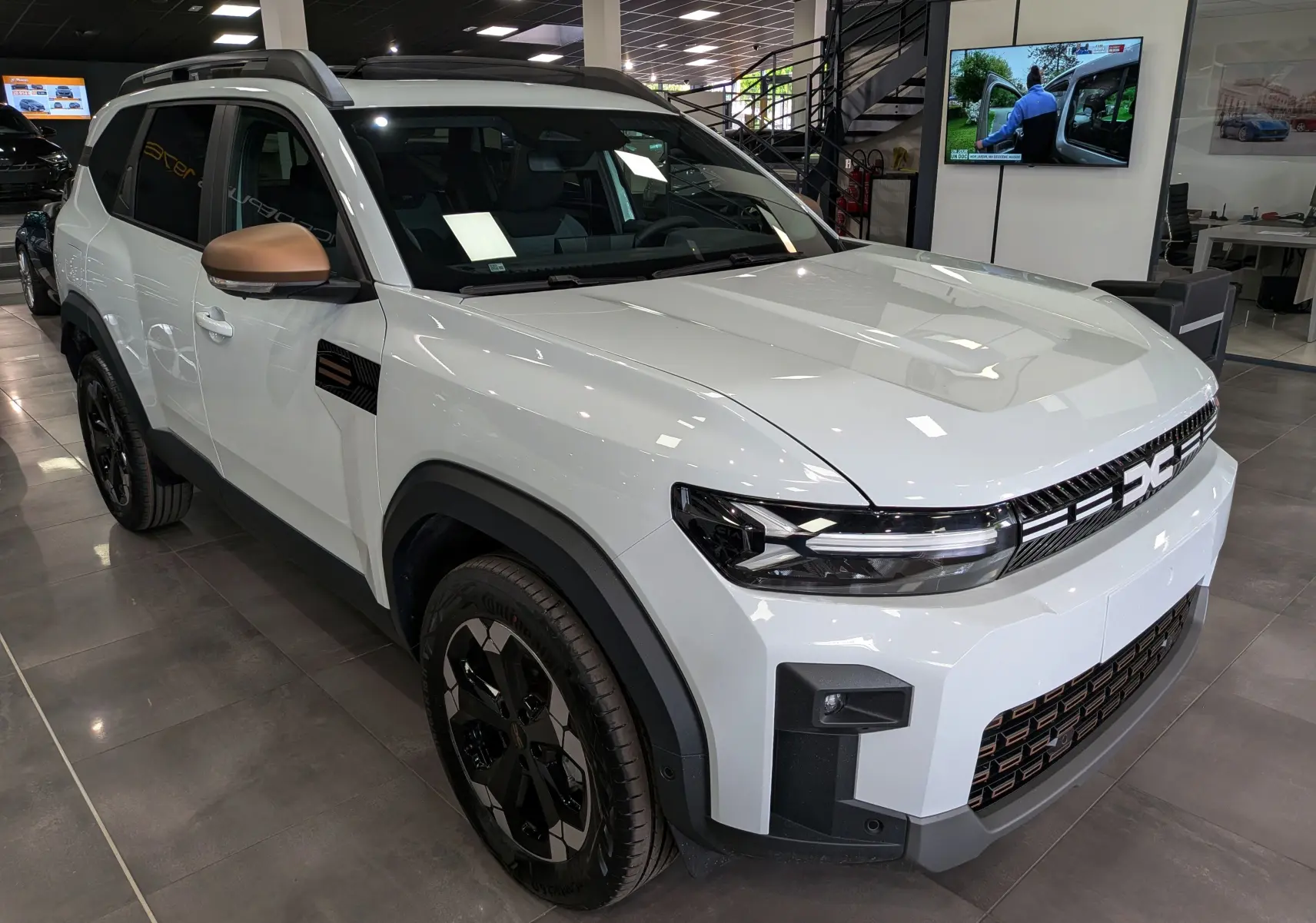 SUV Dacia Bigster blanc glacier en 3/4 avant droit, avec rétroviseurs bronze et jantes noires distinctives.