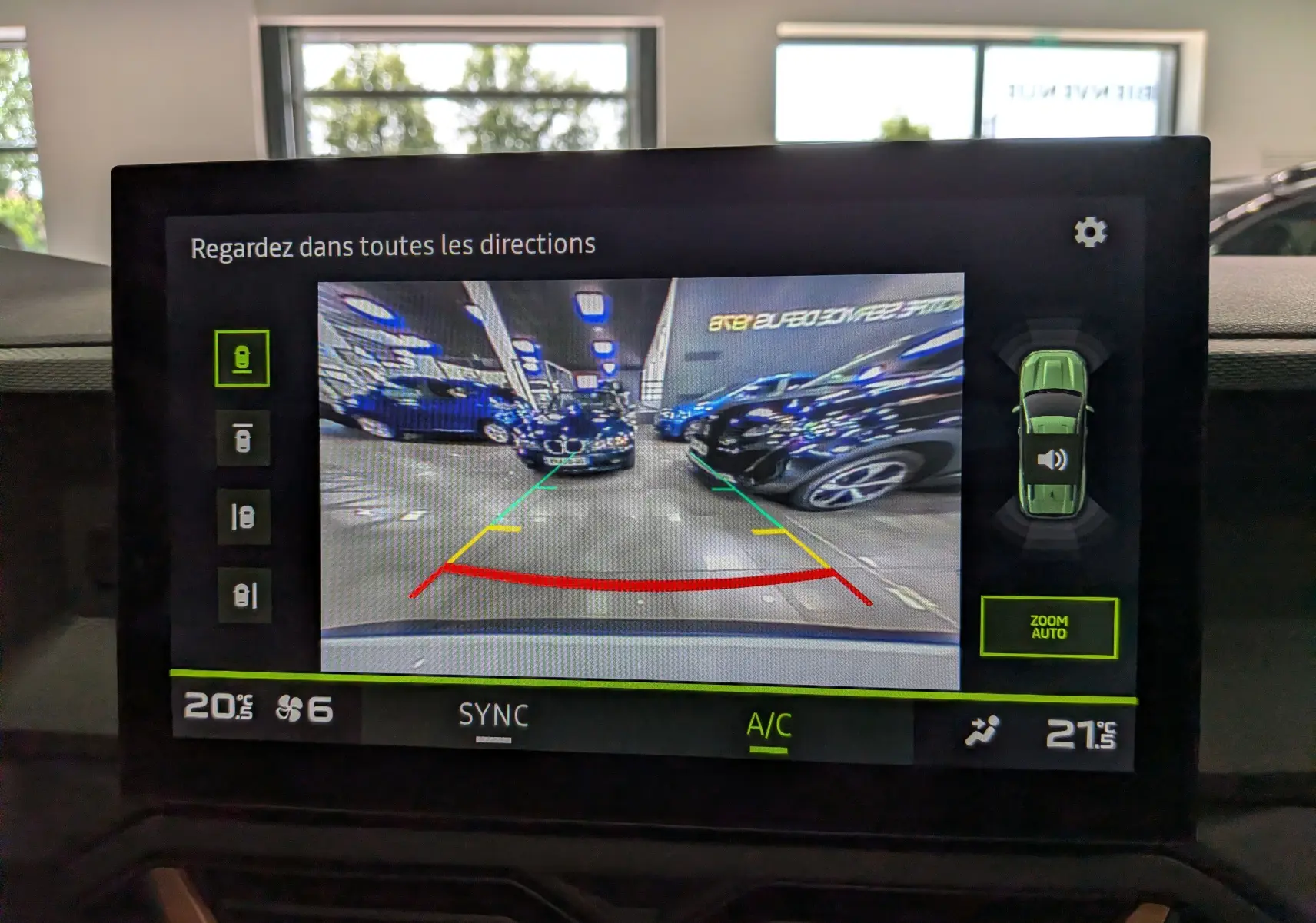 Écran de caméra de recul du Dacia Bigster blanc glacier montrant le parking intérieur avec lignes de guidage colorées.