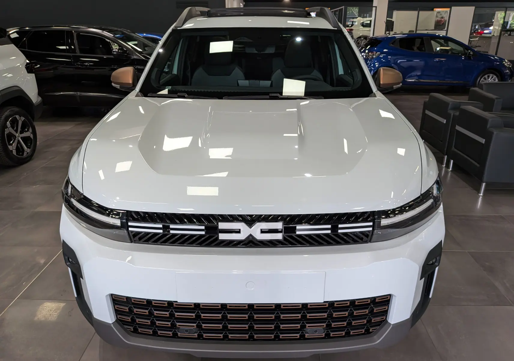 Vue frontale d'un Dacia Bigster blanc glacier avec calandre noire et détails cuivrés en showroom.