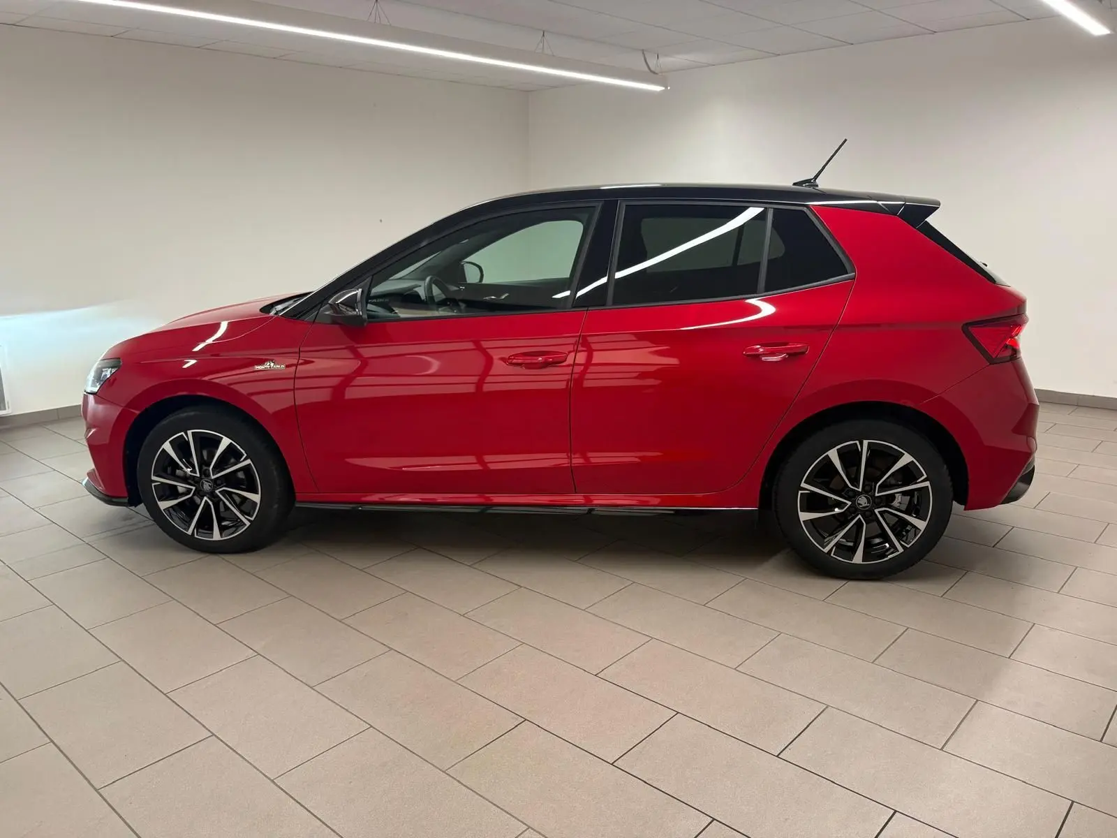 Vue de profil côté gauche d'une Skoda Fabia 2025 rouge Velvet avec toit noir et jantes noires à motifs argentés.