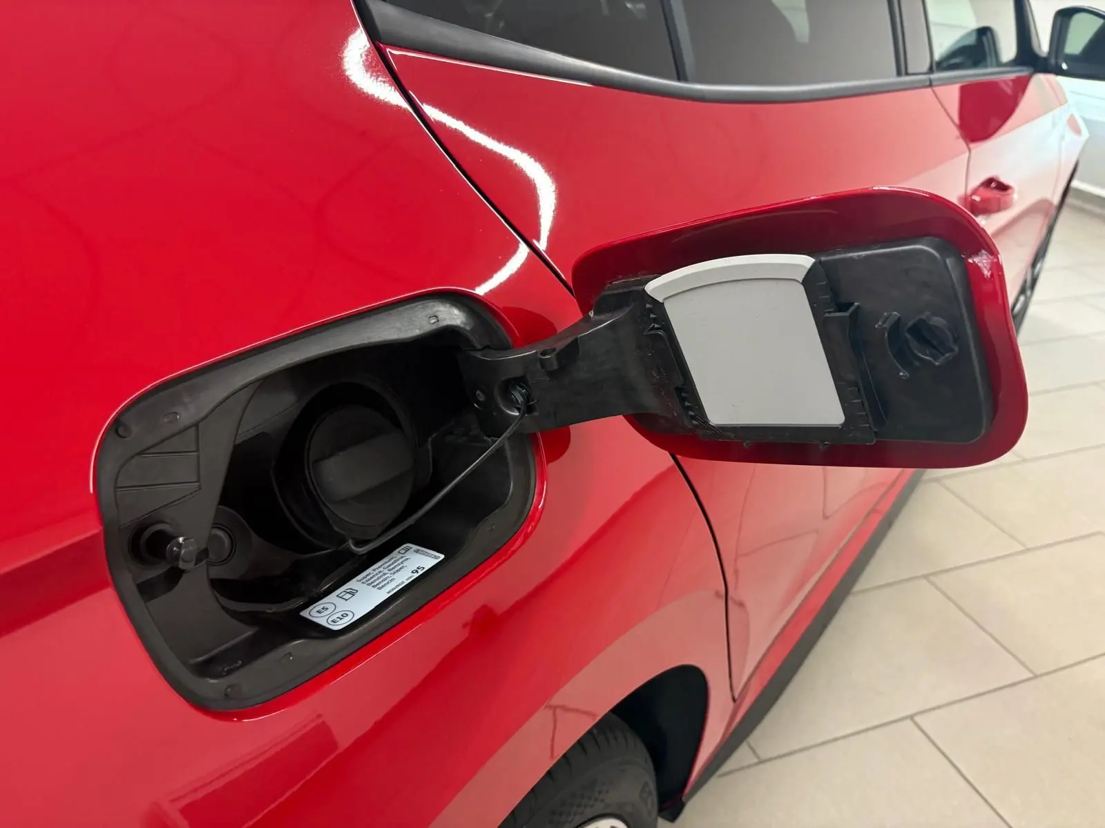 Gros plan sur la trappe à carburant ouverte côté gauche d'une Skoda Fabia rouge Velvet avec toit noir.