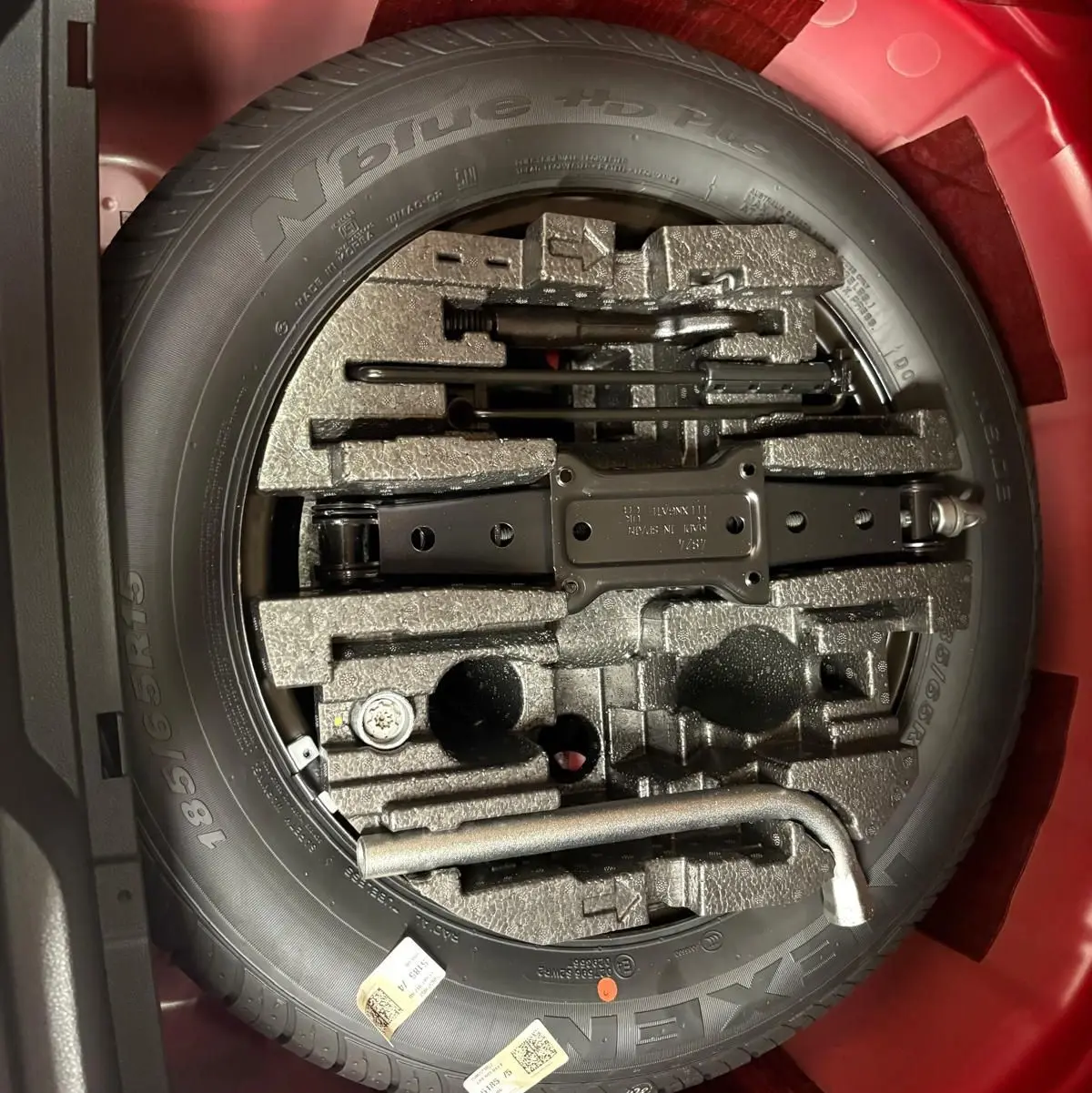 Vue plongeante sur la roue de secours et les outils de bord dans le coffre rouge Velvet d'une Skoda Fabia Monte Carlo 2025.