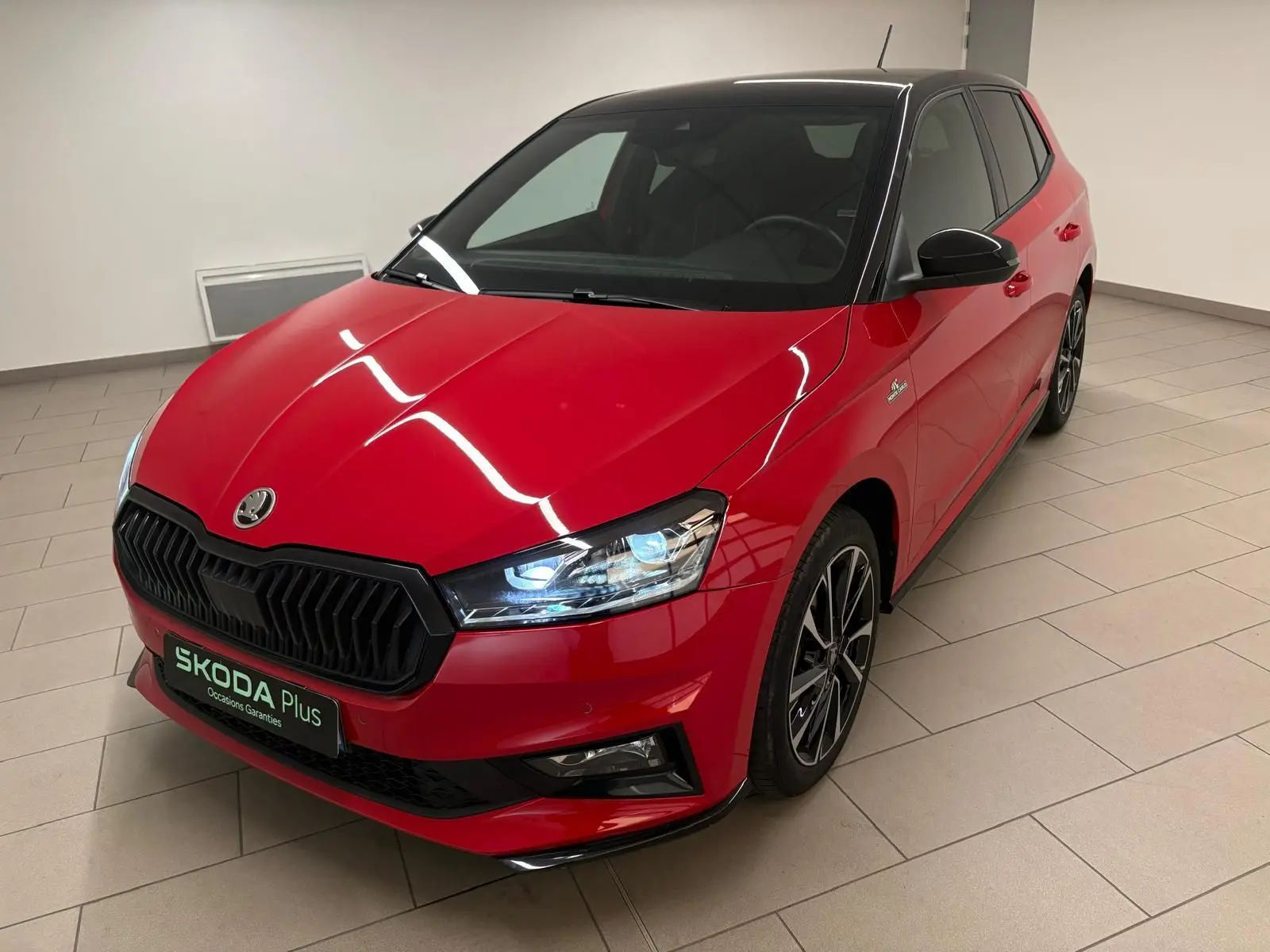 Vue 3/4 avant droite d'une Skoda Fabia Monte Carlo rouge velvet avec toit noir et jantes sport dans un showroom.