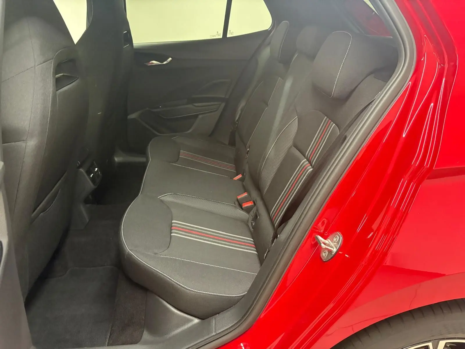 Vue intérieure côté gauche des sièges arrière noirs avec surpiqûres rouges, porte ouverte sur carrosserie rouge velvet.