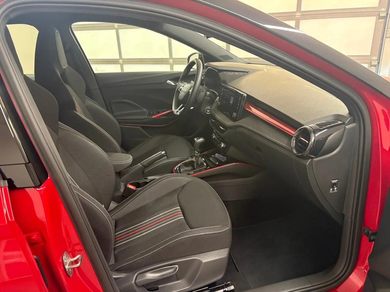Vue intérieure côté conducteur d'une Skoda Fabia rouge velvet avec détails noirs et touches rouges sur tableau de bord et sièges.