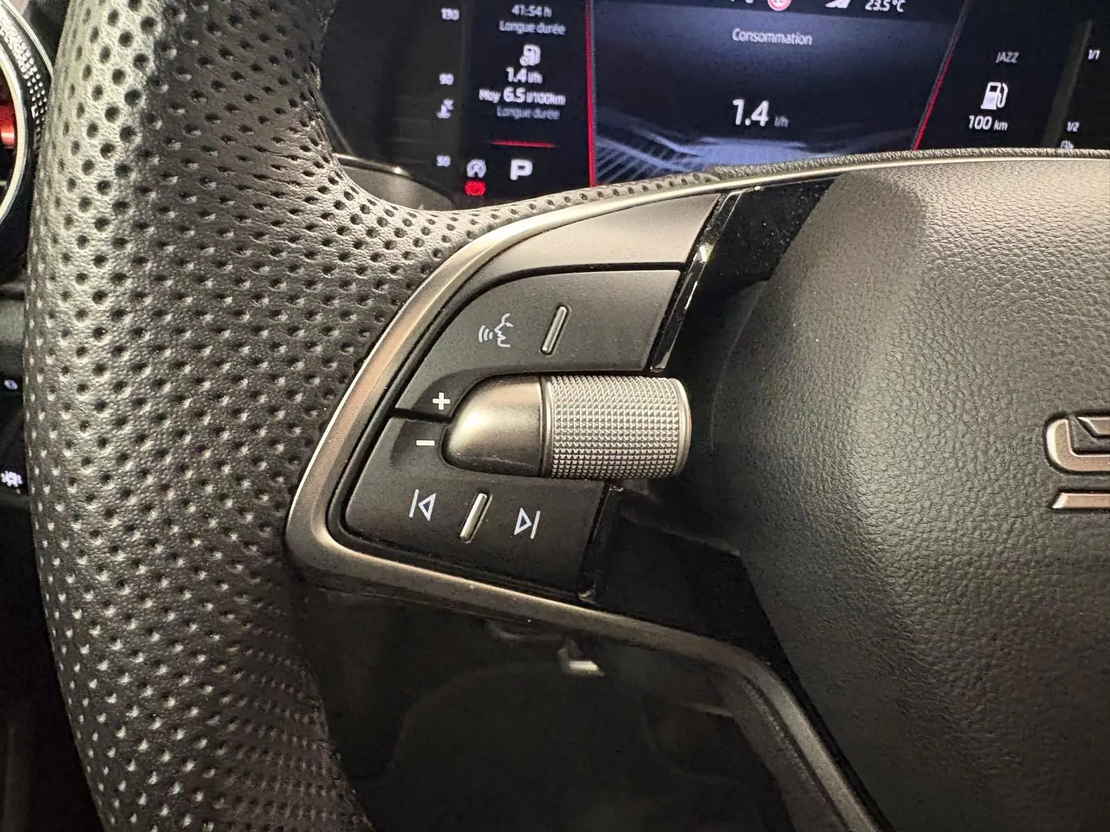 Gros plan sur les commandes gauche du volant perforé d’une Skoda Fabia 2025, avec écran numérique en arrière-plan.