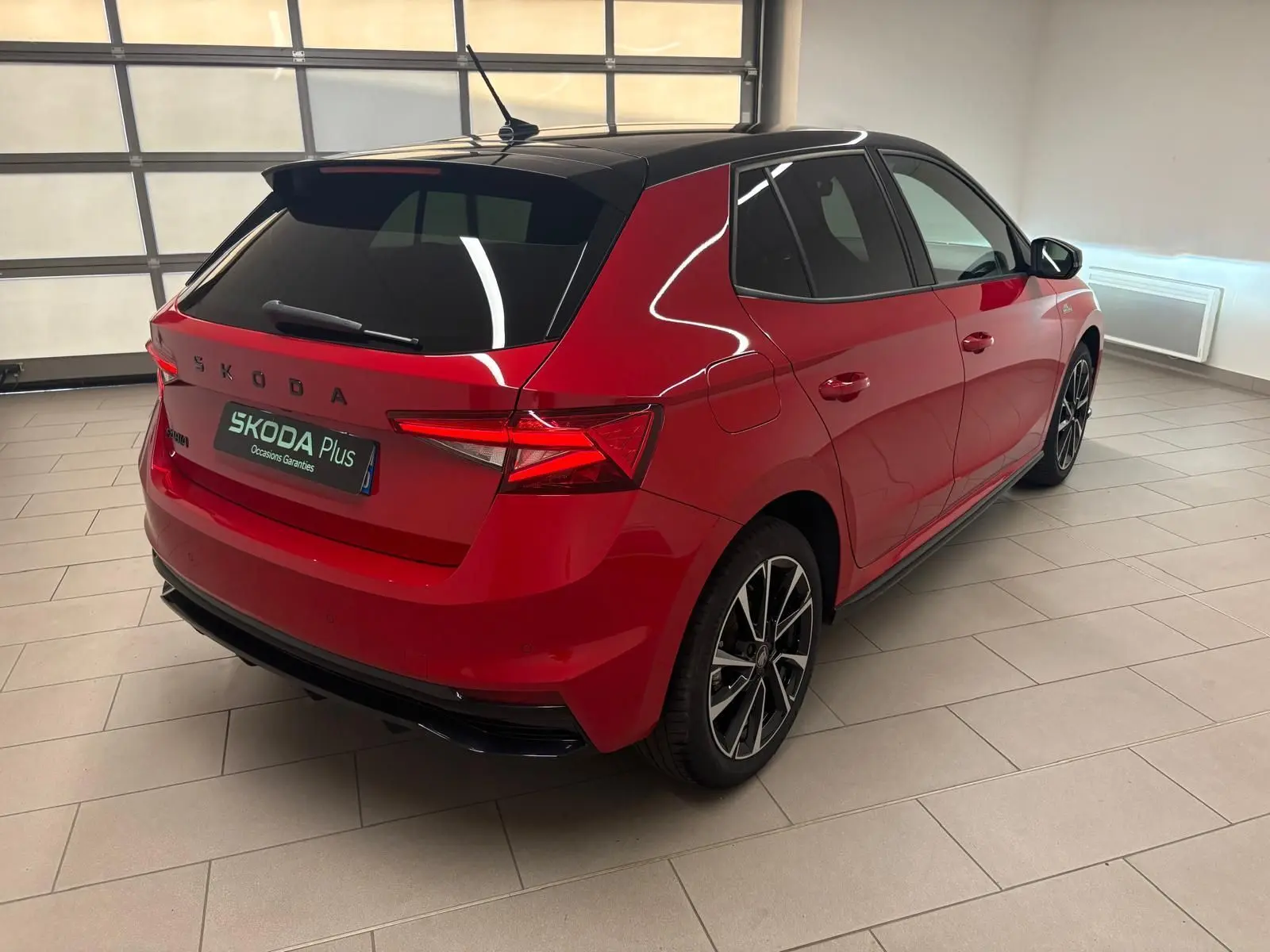 Vue 3/4 arrière droite d'une Skoda Fabia 1.0 TSI Monte Carlo rouge Velvet avec toit noir dans un showroom.