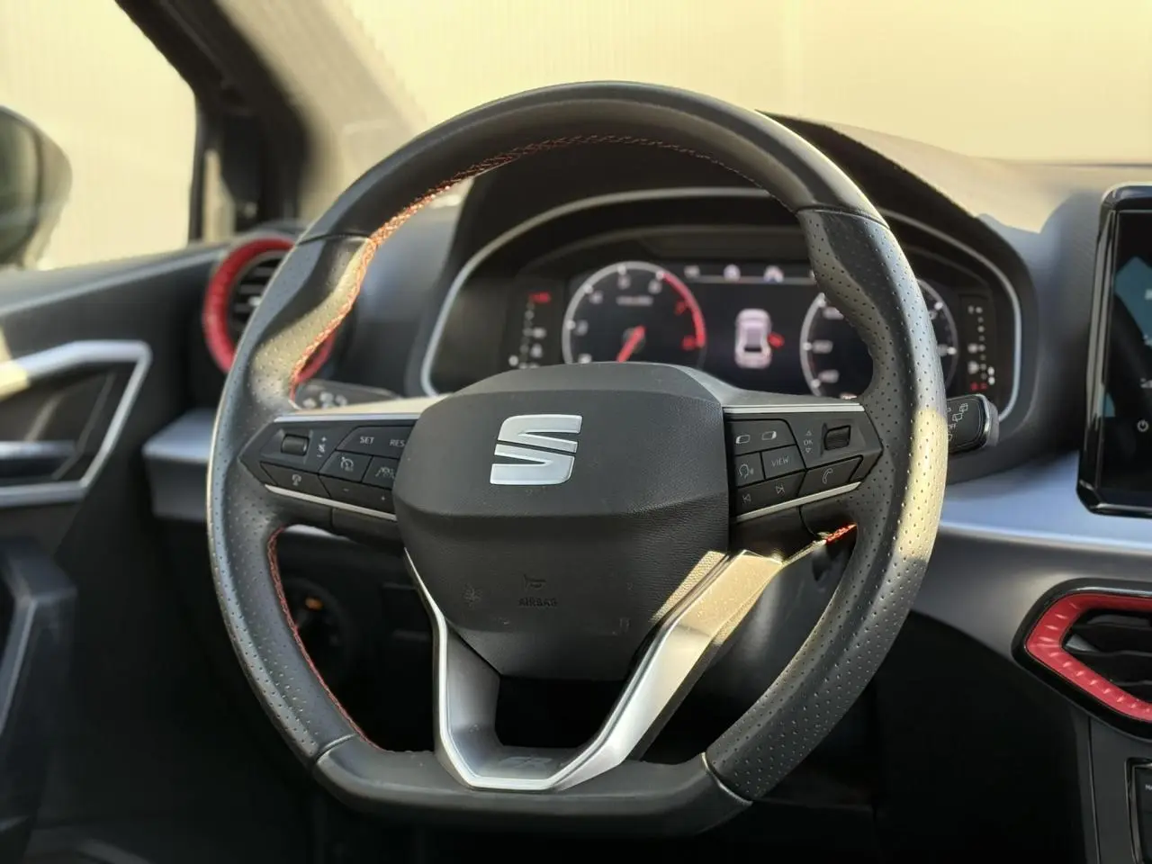 Volant perforé avec logo SEAT au centre, tableau de bord numérique et touches de finition rouge visibles côté conducteur.