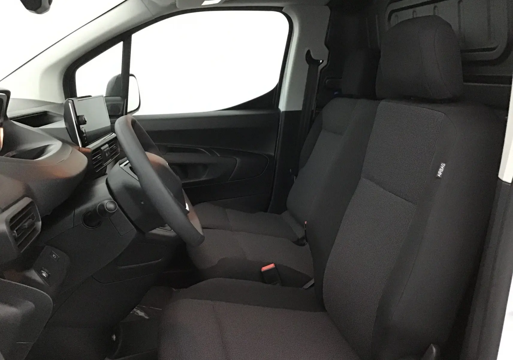 Vue intérieure côté conducteur du Peugeot Partner blanc 2025, montrant les sièges avant noirs et le tableau de bord moderne.