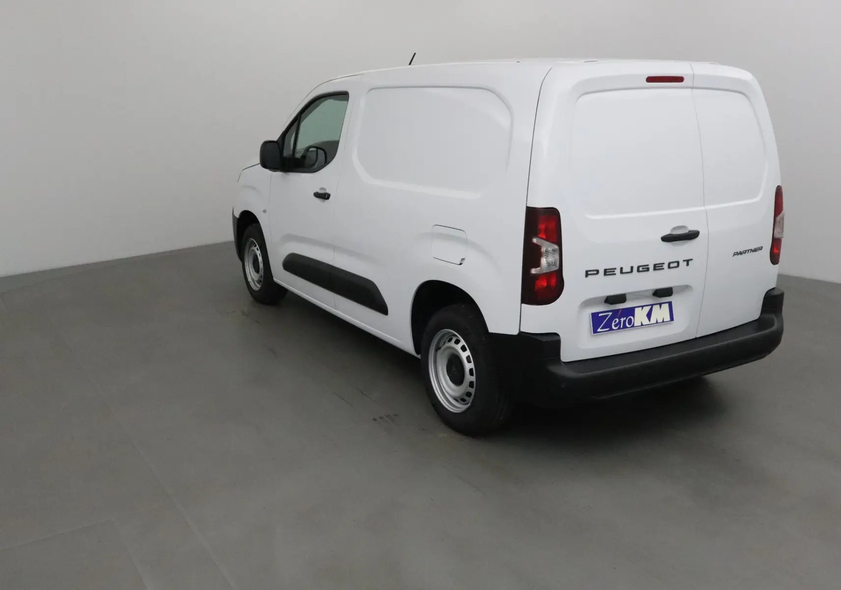 Vue 3/4 arrière droite du Peugeot Partner blanc 2025, fourgon utilitaire avec détails noirs sur les bas de caisse.