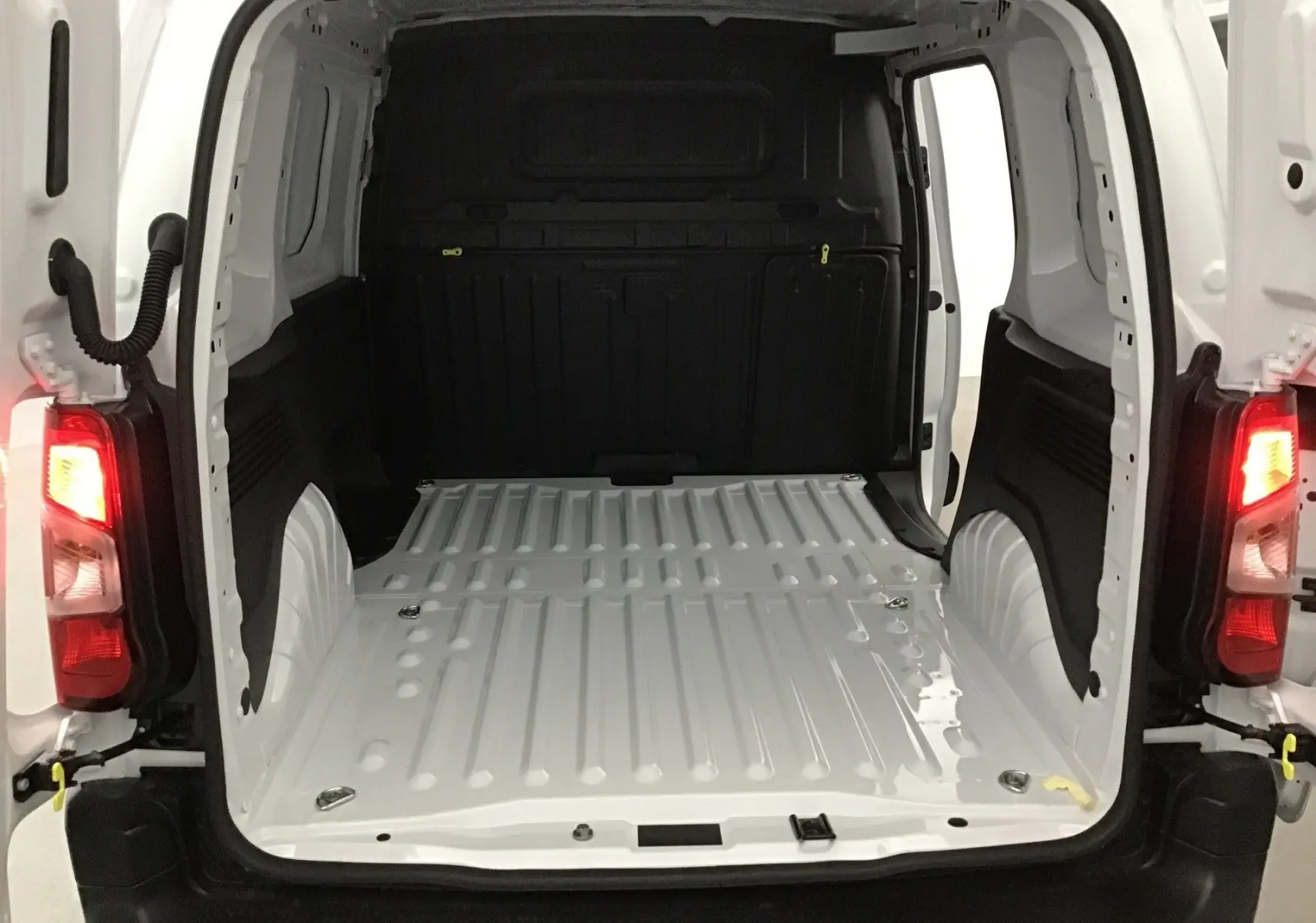 Vue arrière du Peugeot Partner blanc 2025, montrant l'espace de chargement vide avec portes arrière ouvertes et feux allumés.
