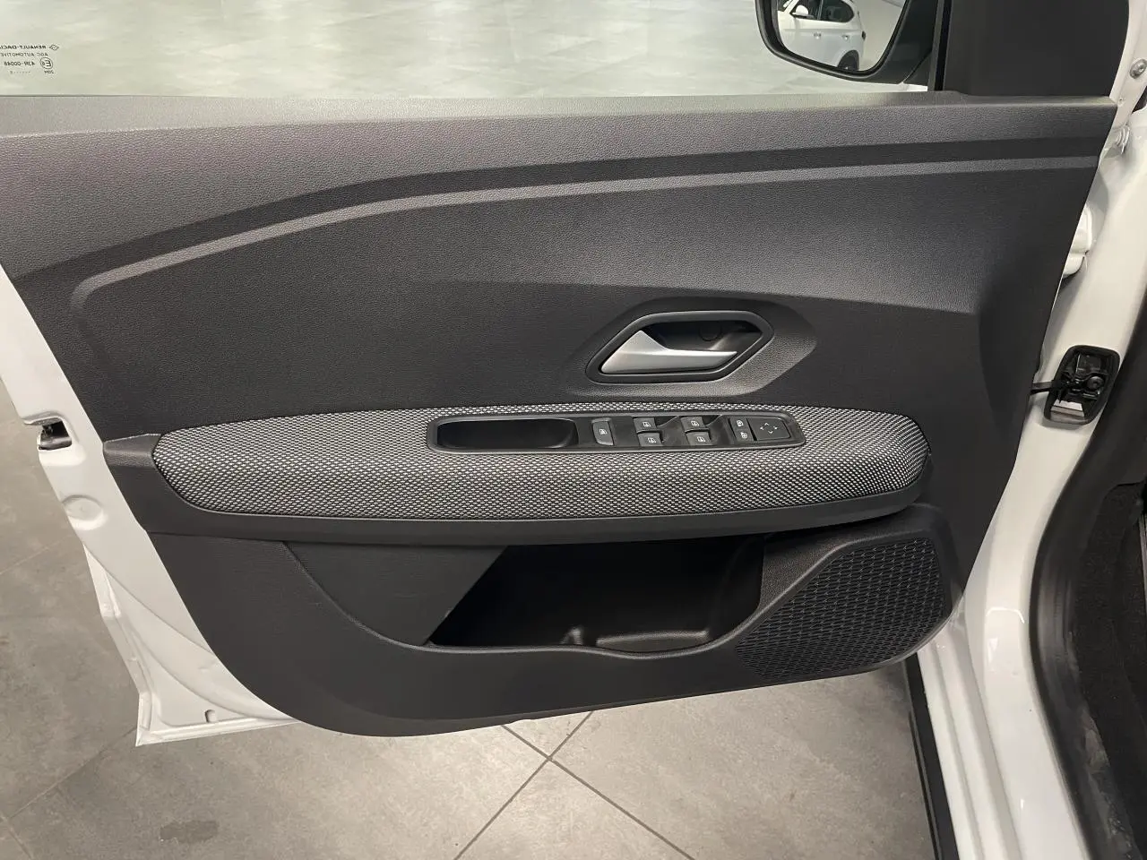 Vue intérieure de la porte avant gauche blanche glacée de la Dacia Sandero Stepway avec commandes de vitres et poignée grise.