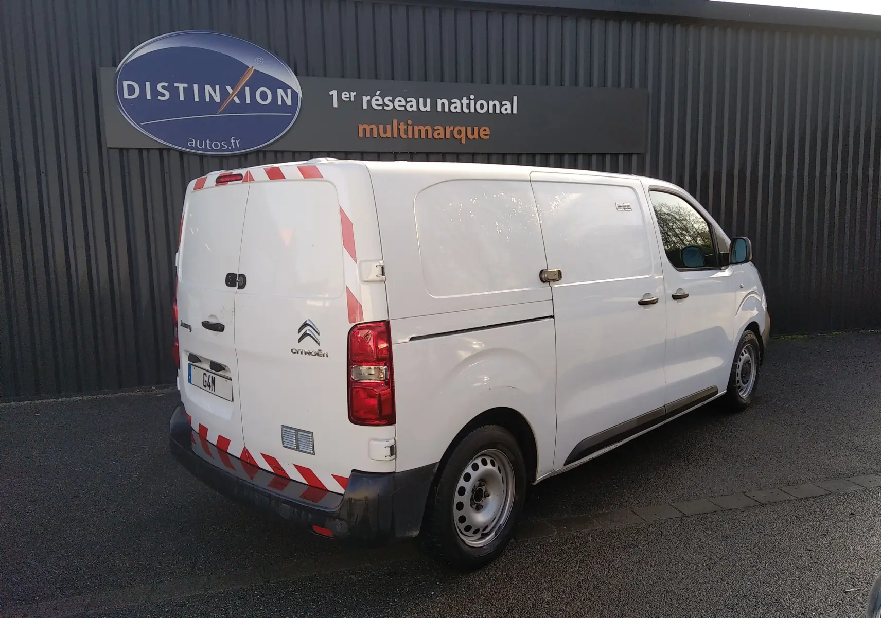 Vue 3/4 arrière droite d’un Citroën Jumpy blanc fourgon 2021 avec bandes réfléchissantes rouges et blanches sur la porte arrière.