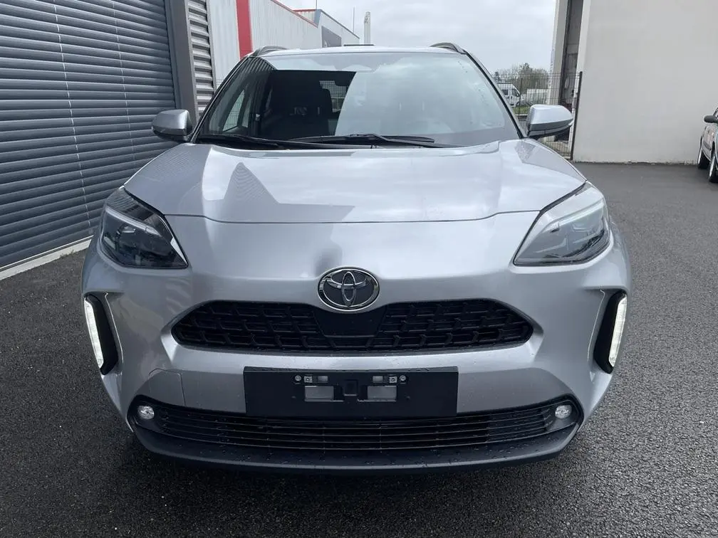 Vue frontale d'une Toyota Yaris Cross gris clair avec calandre noire et feux diurnes verticaux allumés.
